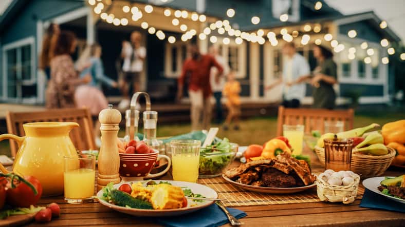 Backyard Dinner Table with Tasty Grilled Barbecue Meat, Fresh Vegetables and Salads. Happy Joyful People Dancing to Music, Celebrating and Having Fun in the Background on House Porch. best wireless meat thermometers