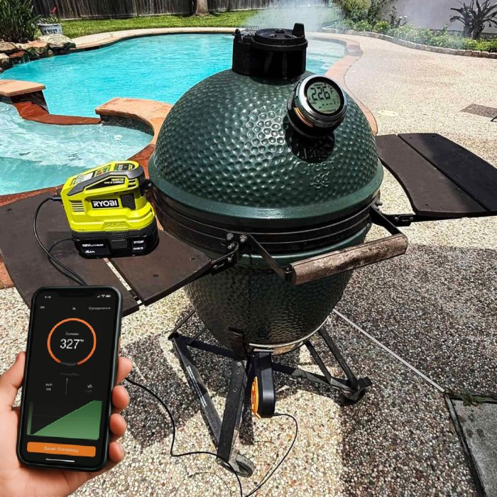 Wireless smart thermometer on a barbecue grill with smartphone app display for precise temperature monitoring.