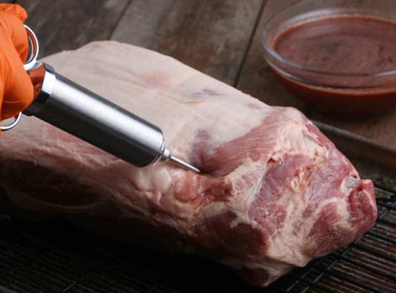 1. Syringe injecting marinade into raw pork shoulder for smoking or BBQ.