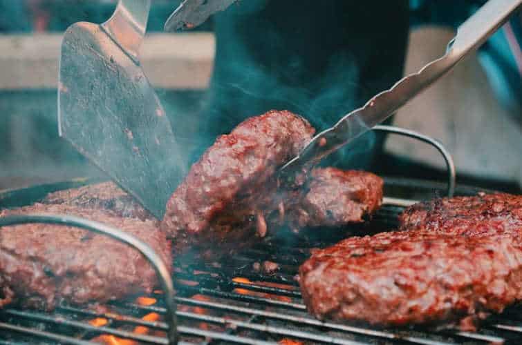Grilling juicy steaks on a barbecue grill with tongs and spatula at a cookout.