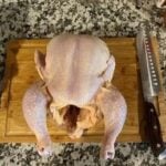 Raw whole chicken on cutting board for cooking or roasting.