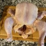 Raw whole chicken on cutting board ready for cooking.