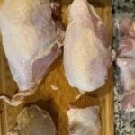 Raw chicken pieces on a wooden cutting board for food prep.