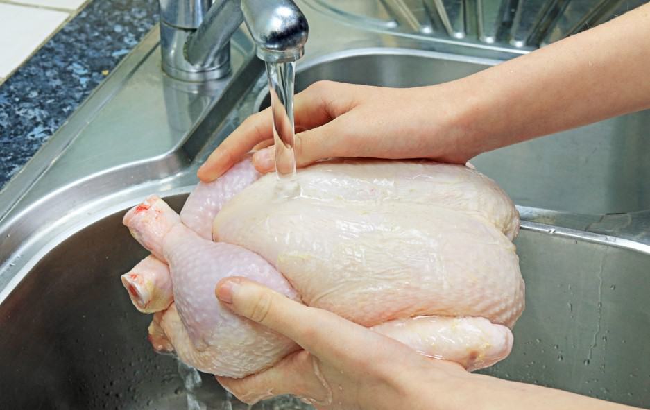 Fresh raw chicken being washed under running water for food safety and hygiene.